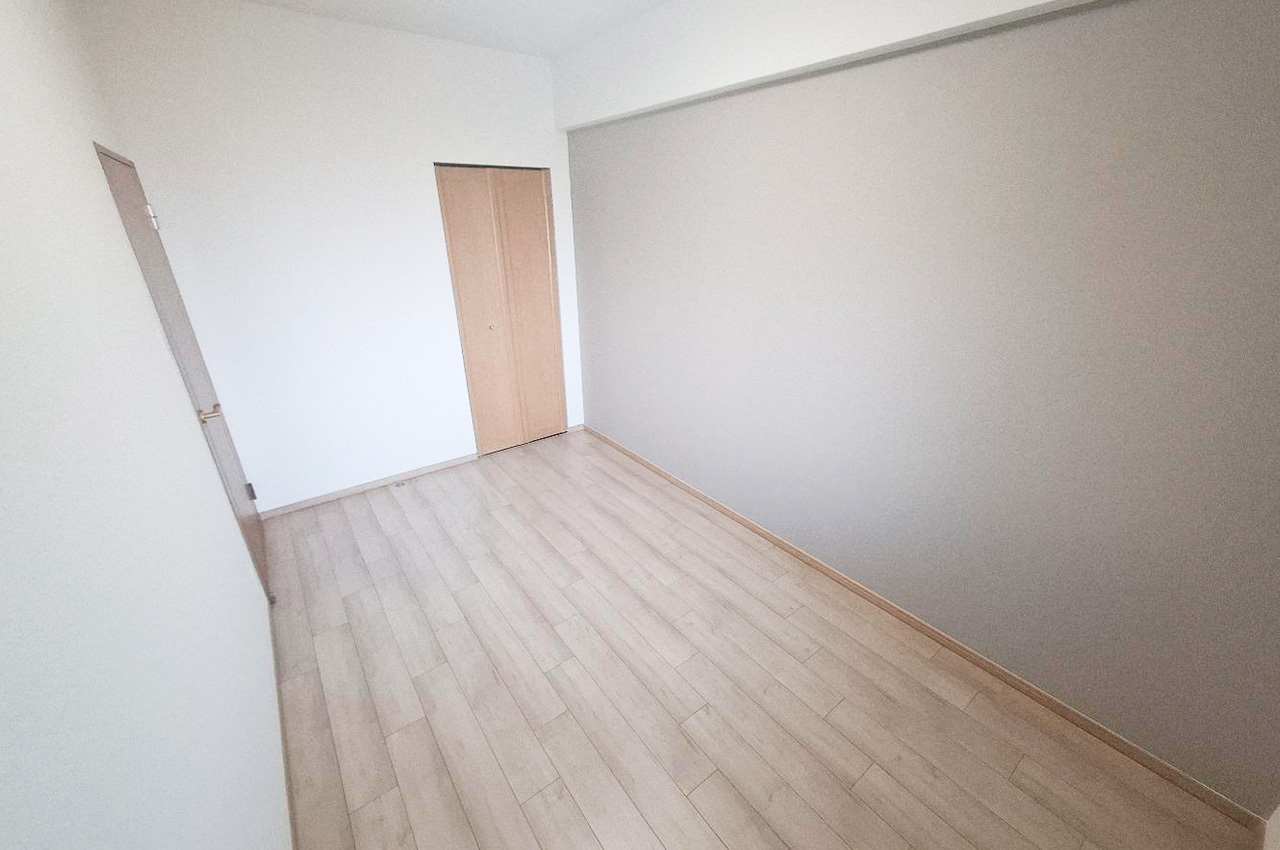 洋室:リフォーム済みのナチュラルな床とグレーのアクセントクロスが調和するシンプルで上質な空間。